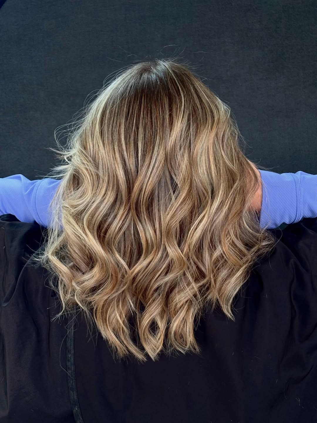 Back view of shoulder-length bronde hair with honey blonde pieces and defined waves