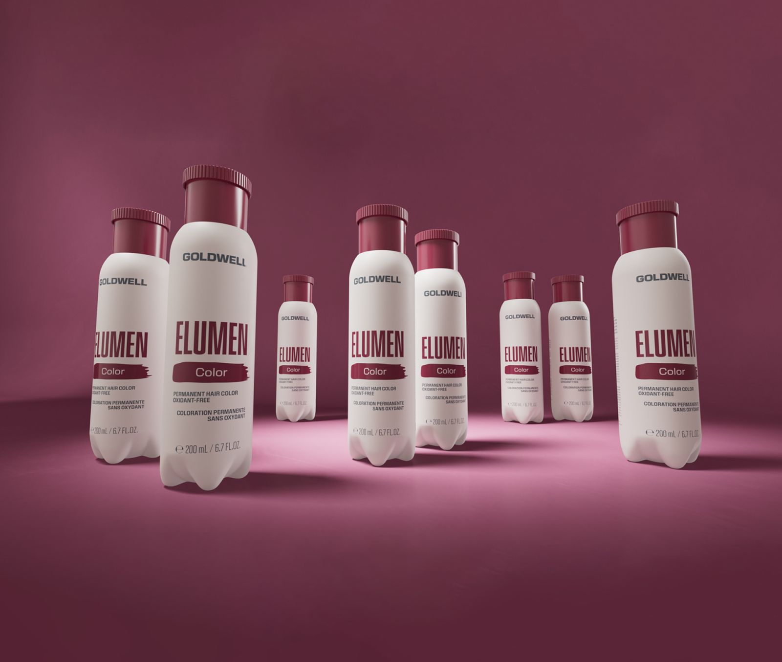 Goldwell Elumen bottles, white with burgundy caps, arranged on a magenta studio floor. Product photo.