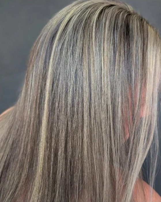 Close view of fine blonde highlights woven through brunette hair at the part on a real client