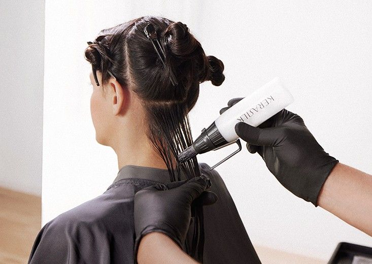 Kerasilk brand photo: a stylist works the keratin formula onto a parted section of dark hair using an applicator bottle