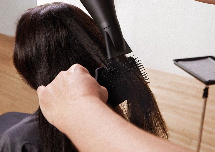 Kerasilk brand photo: a stylist blow-drying long dark brown hair straight with a paddle brush