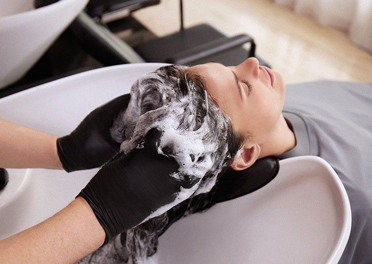 Kerasilk brand photo of gloved hands working shampoo into a lather at the backwash basin