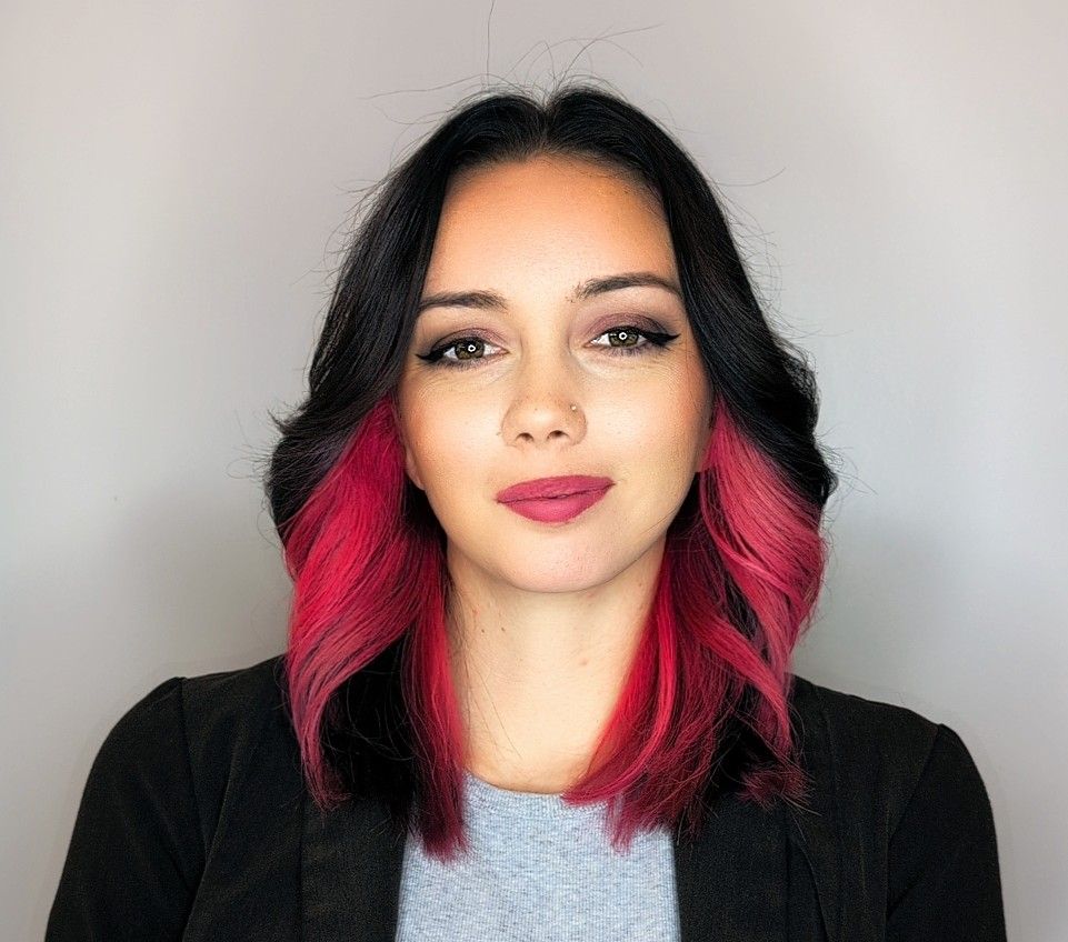 Portrait of Vanessa, hair stylist at Hair Goddess Salon, Spa & Boutique, with dark hair and her own vivid pink color underneath